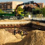 Construction workers operating at an urban site in Madrid, with machinery and residential buildings in view.