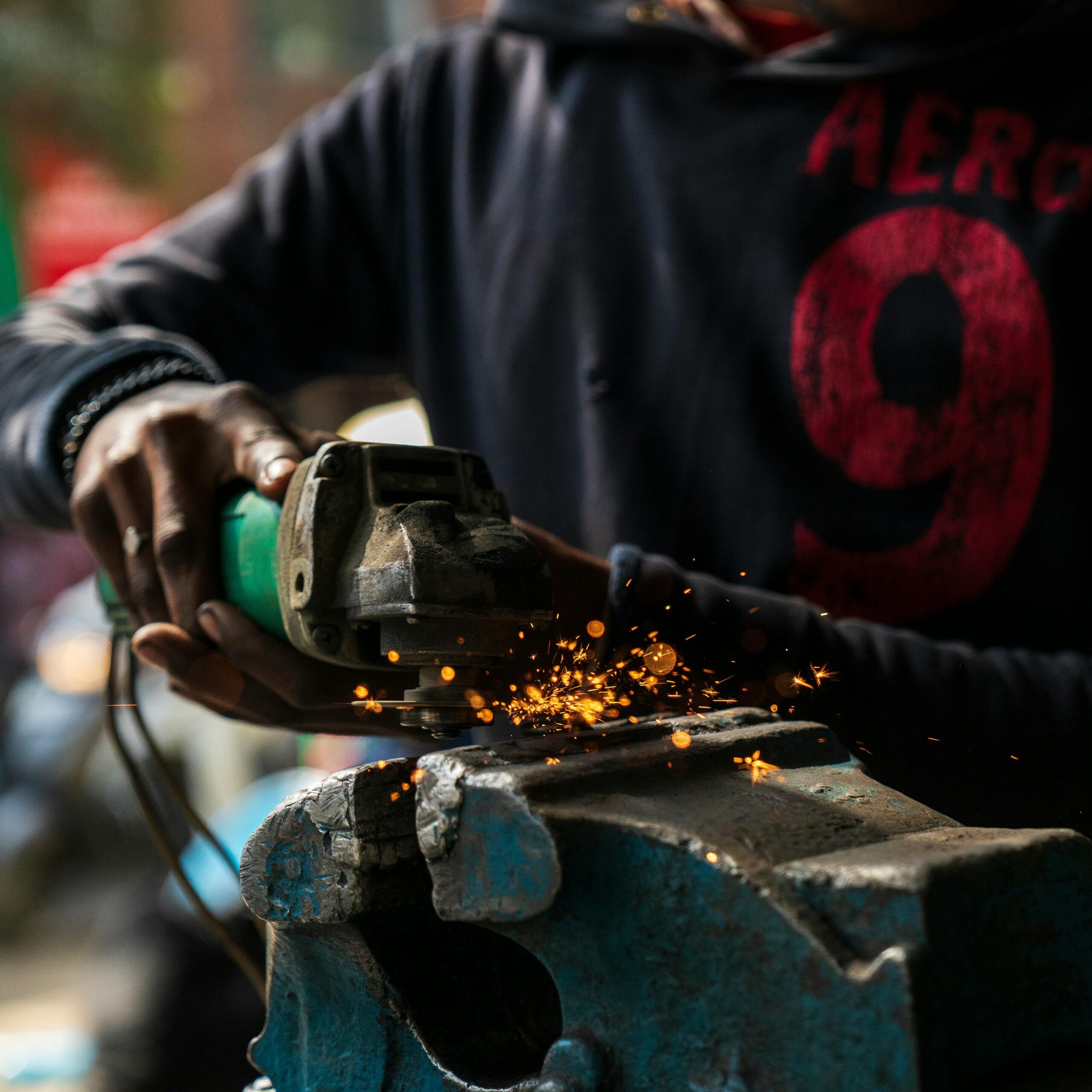 Crop anonymous African American male worker in dirty wear welding metal details in blurred factory