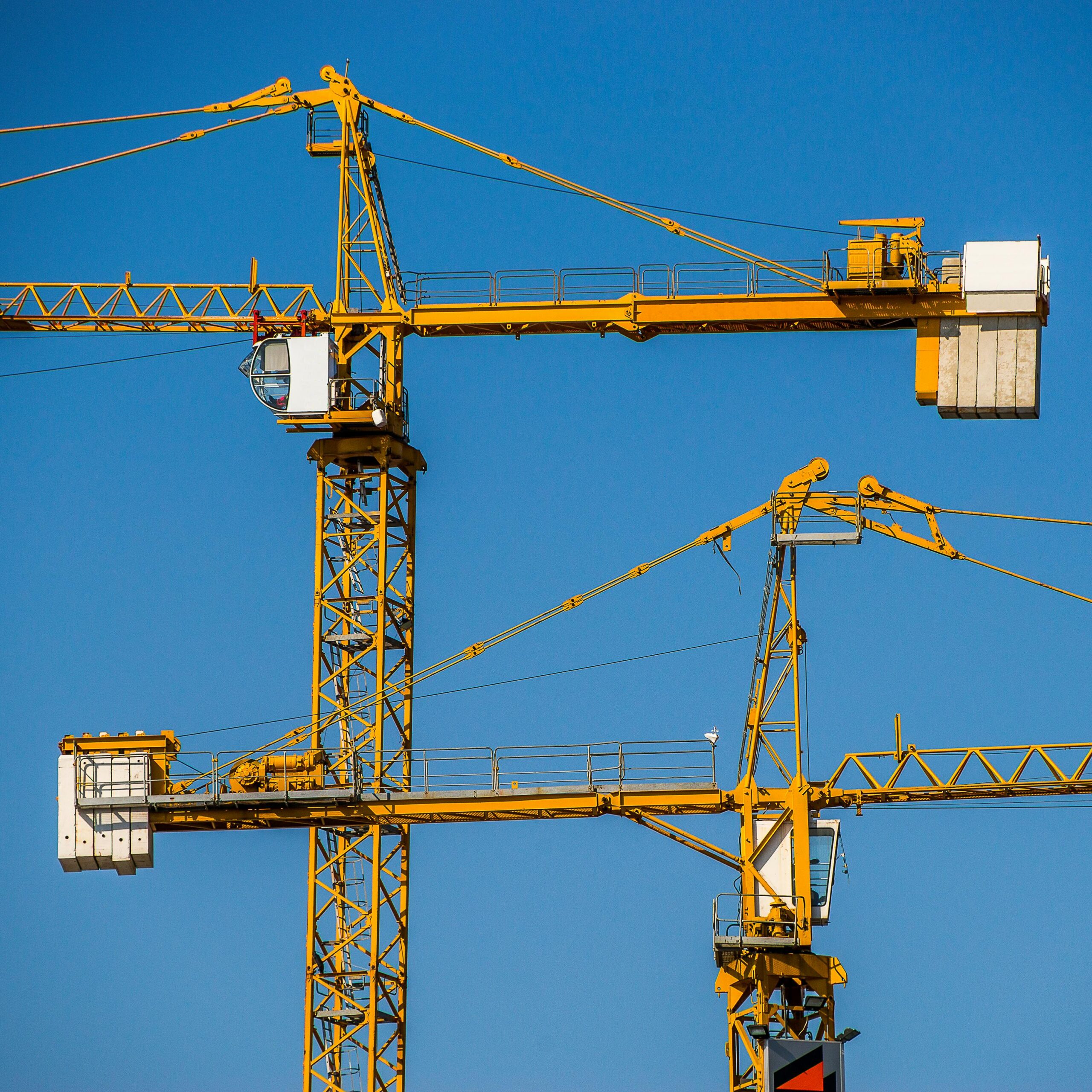 Two yellow tower cranes towering against a clear blue sky at a construction site.